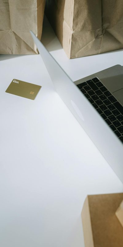 A laptop with a credit card, surrounded by paper bags, illustrating online shopping.