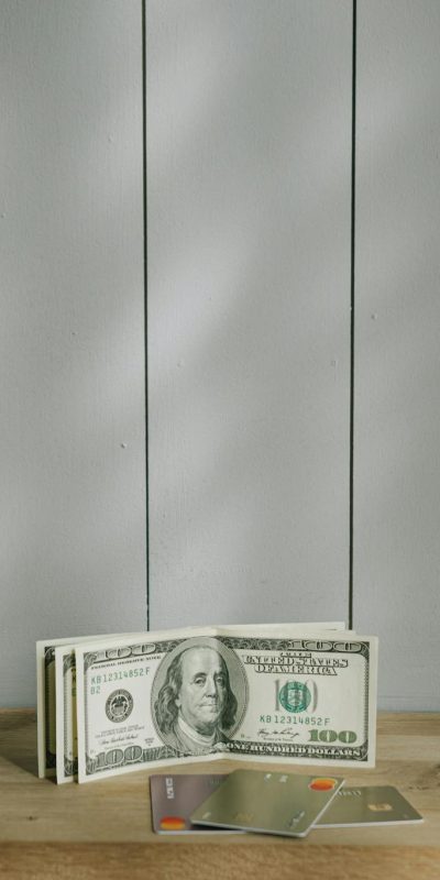 A stack of hundred-dollar bills and credit cards on a wooden surface with a neutral background.
