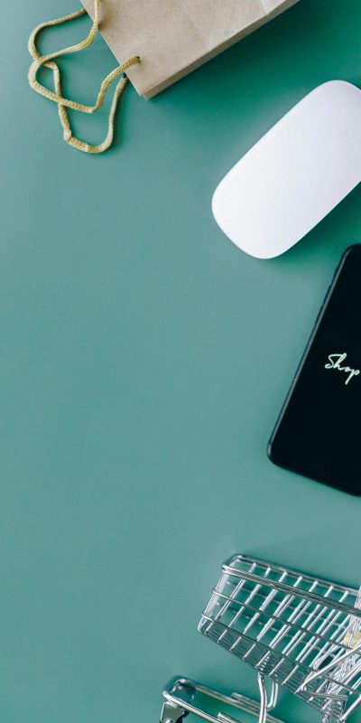 Flat lay of a smartphone, shopping cart, and paper bag representing online shopping and e-commerce.