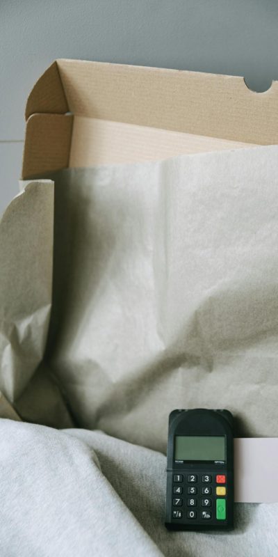 Image of a payment terminal with a cardboard box and paper, representing online shopping and contactless payment.